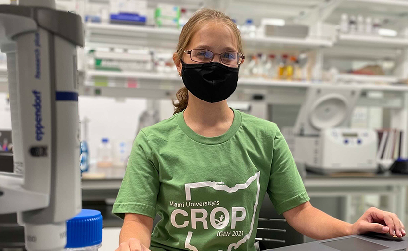 Daria sitting in lab with a black mask on.